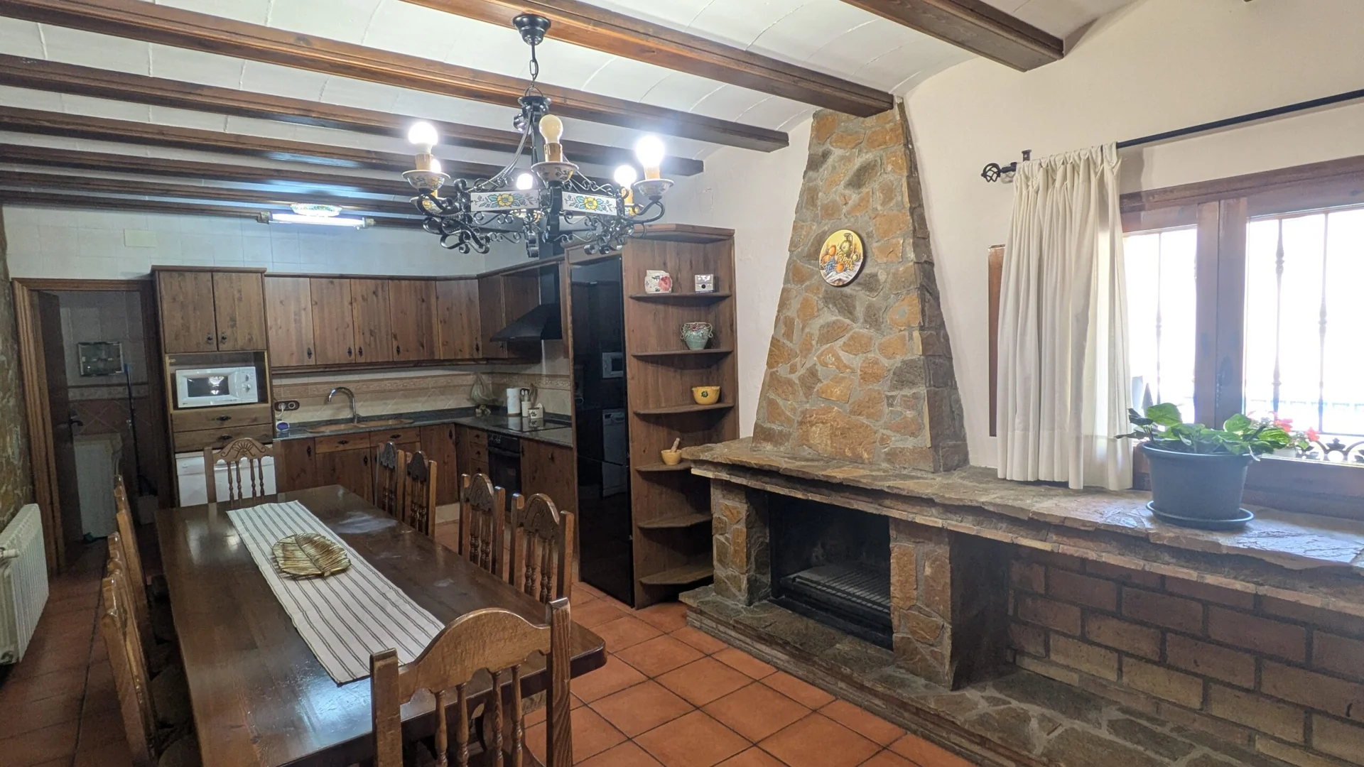 Cocina y comedor con mesa de madera, vigas vistas y chimenea